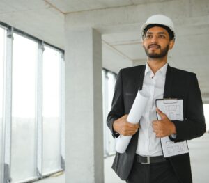 architecture, construction business and building concept – happy smiling indian male architect in helmet.